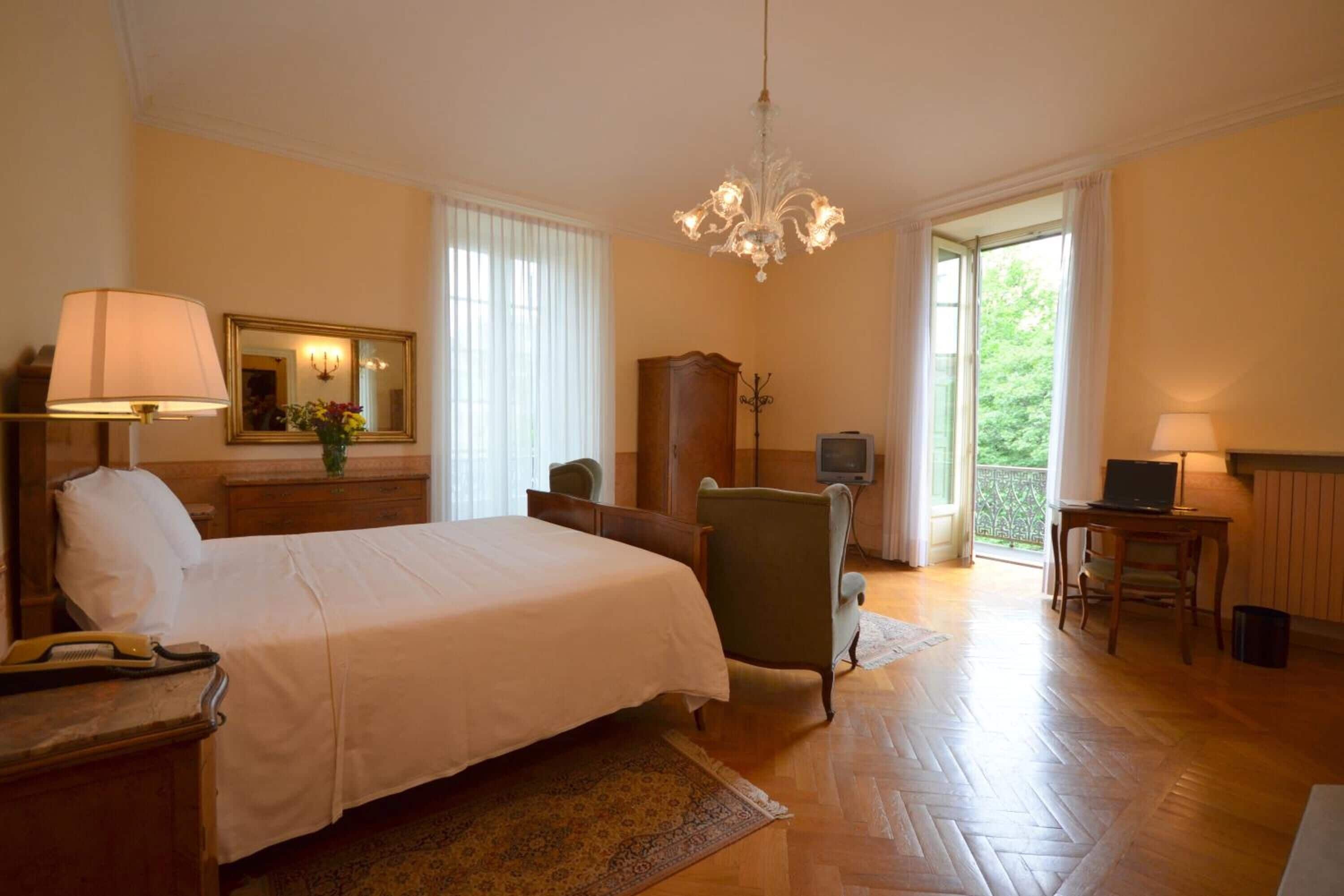 A bedroom with a bed, a desk, a chair, a TV, and a chandelier.