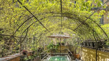 Un patio exterior con mesa y sillas para comer, rodeado de abundante vegetación y una piscina.