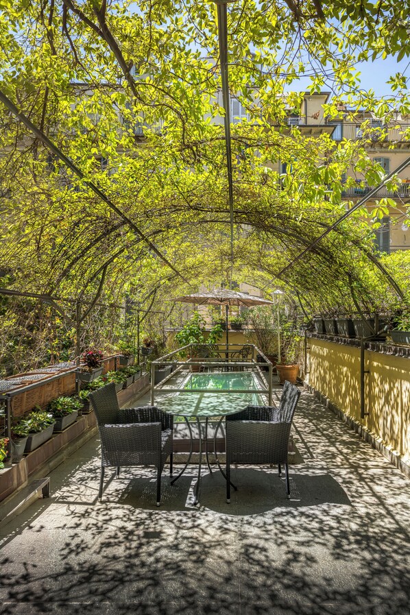 An outdoor patio with a dining table and chairs, surrounded by lush greenery and a pool.