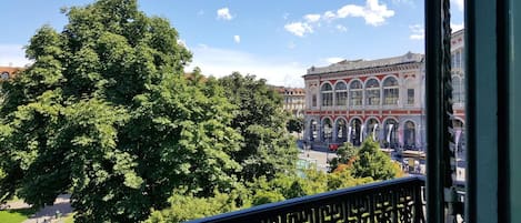 A balcony with a view of a large tree and a historic building with arched windows.