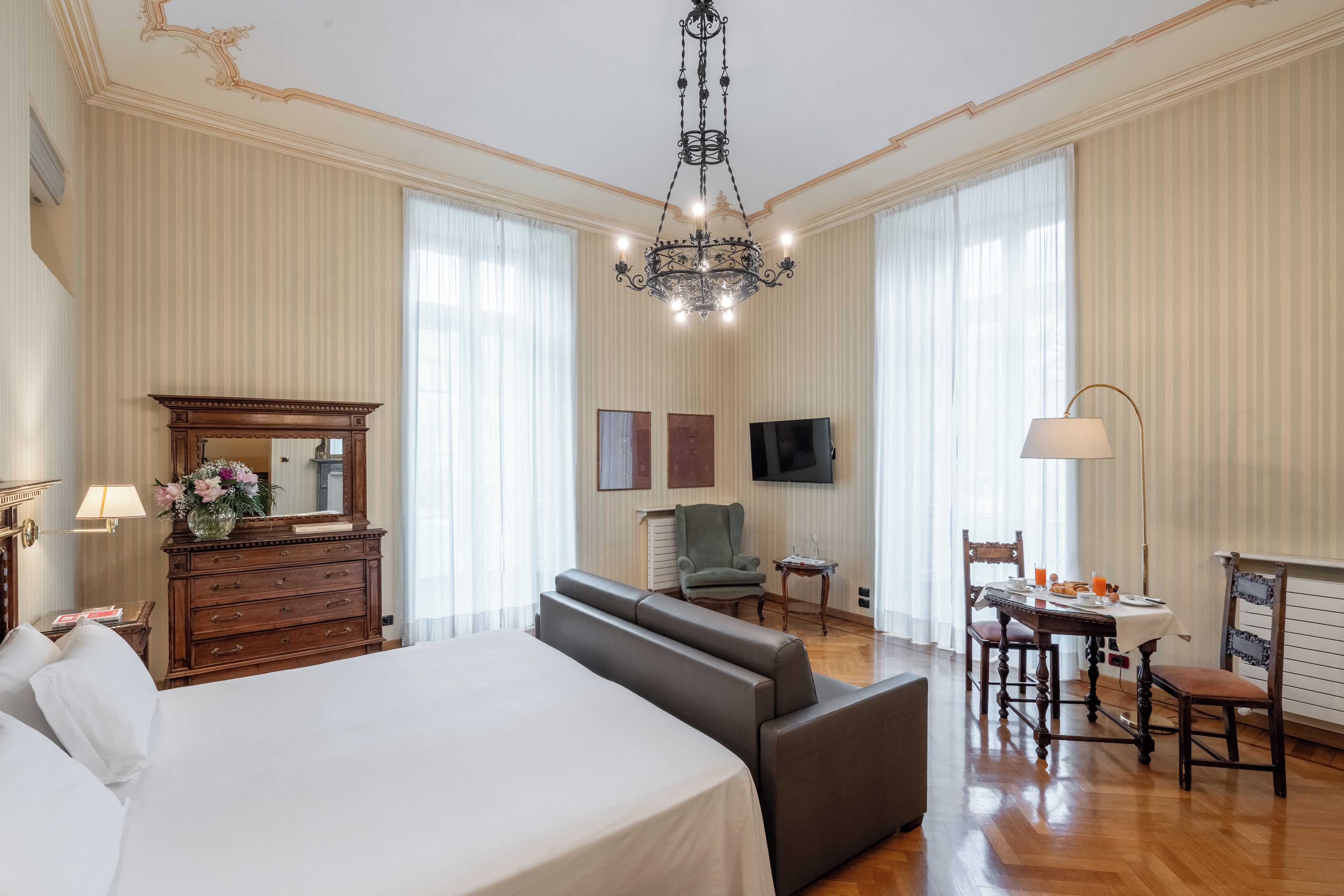 Una camera d'albergo con un letto grande, un divano, un tavolo da pranzo con sedie, una televisione e un lampadario.