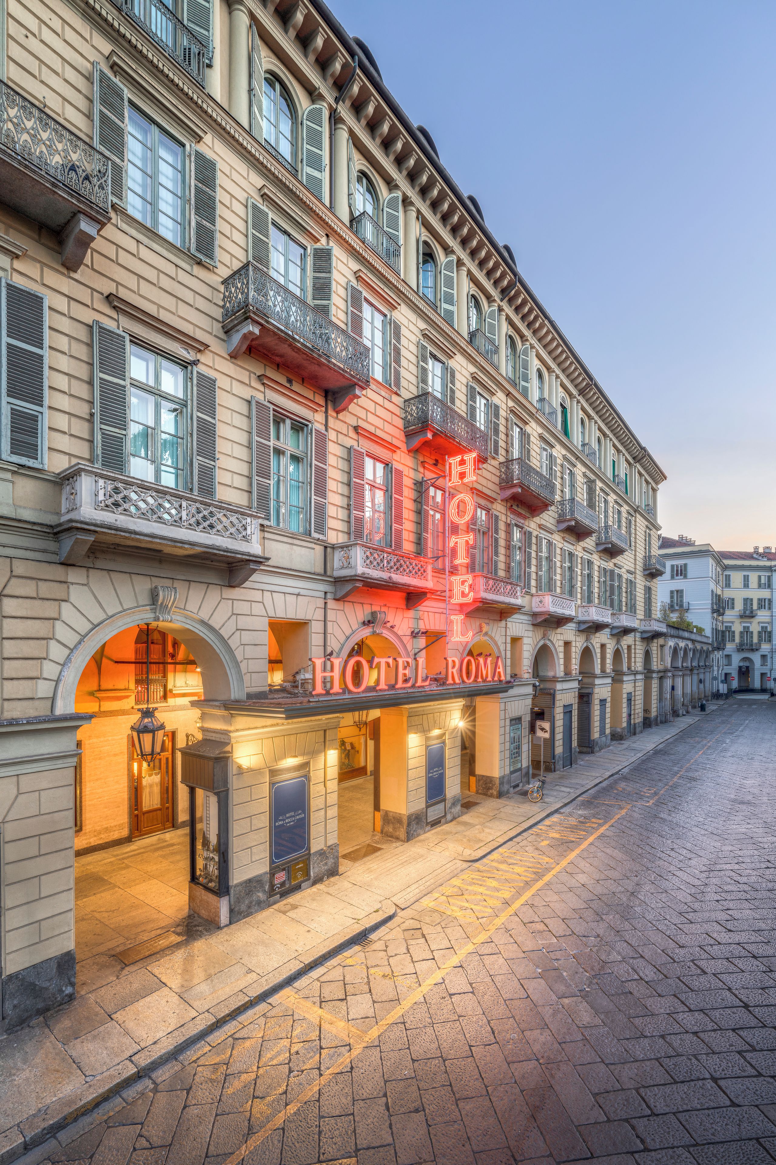 Un edificio histórico con un cartel de hotel destacado, ventanas en arco y una calle adoquinada.