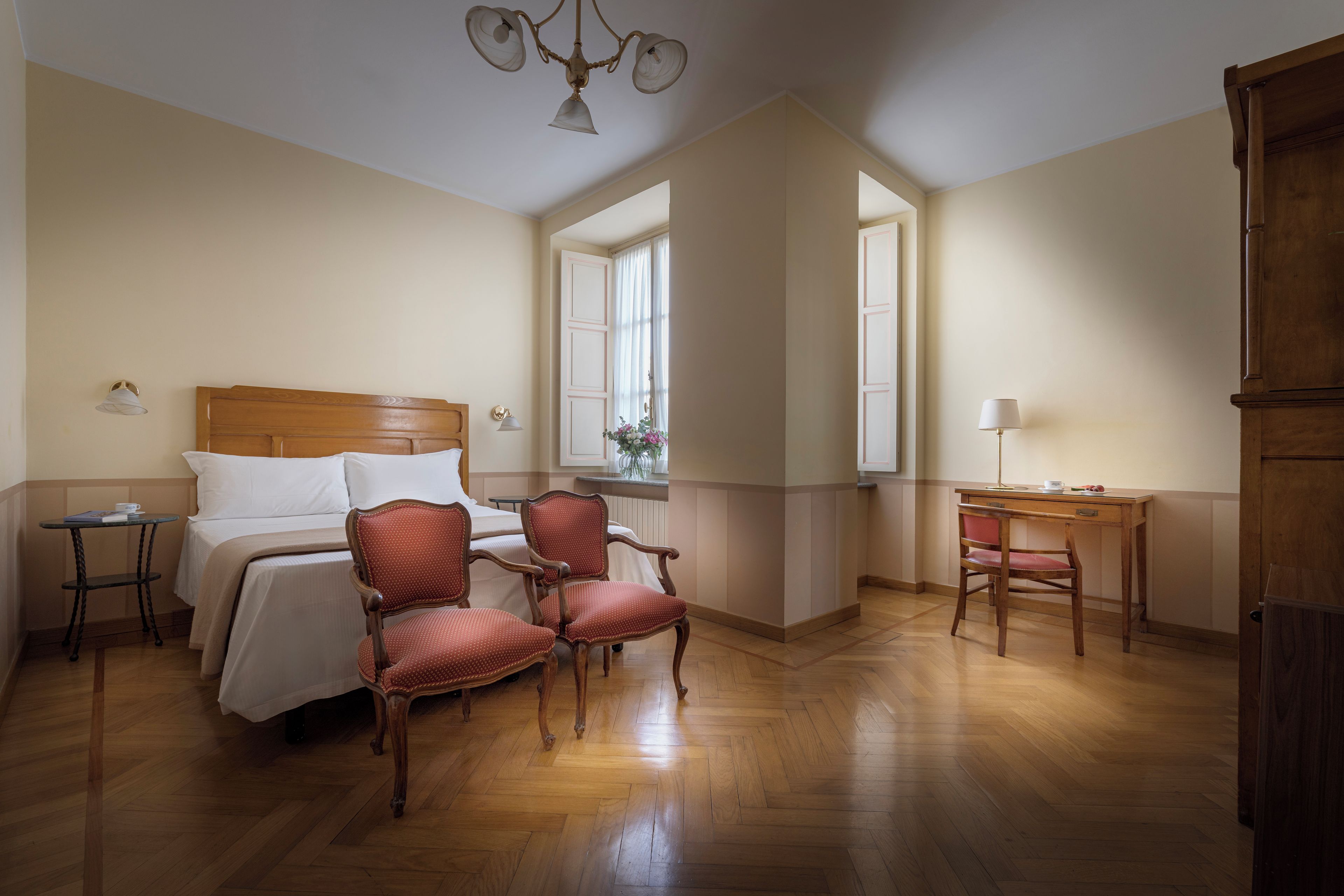 A hotel room with a bed, two chairs, a desk, and a chandelier.