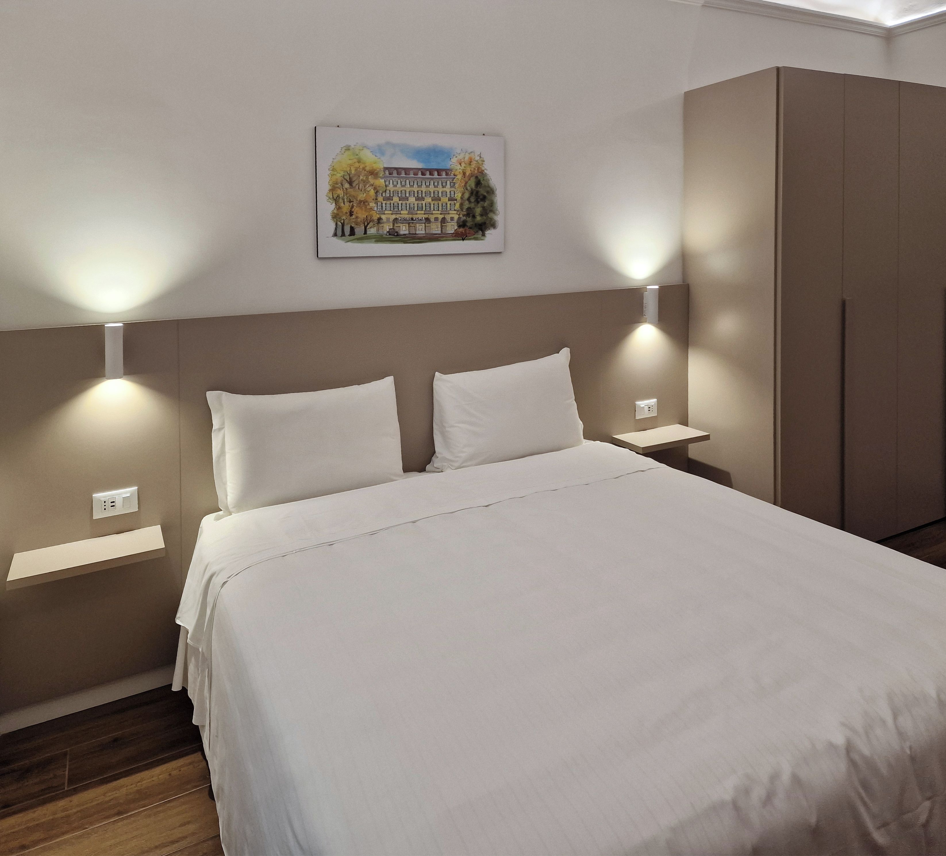 Une chambre d’hôtel comprenant un lit, deux tables de chevet, une armoire et un tableau accroché au mur.