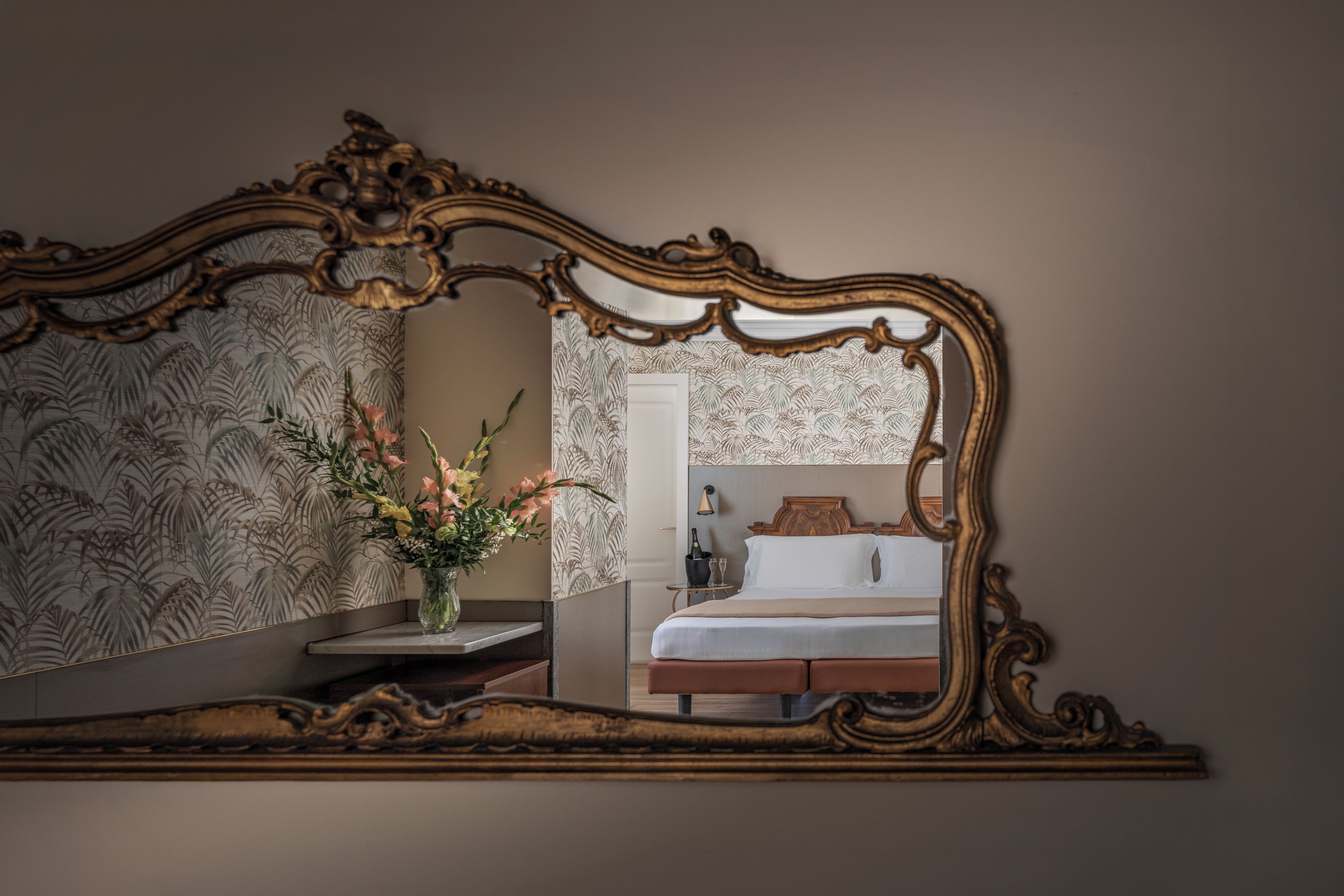 Una camera da letto con uno specchio grande e decorato, un letto, un comodino e un vaso con fiori.