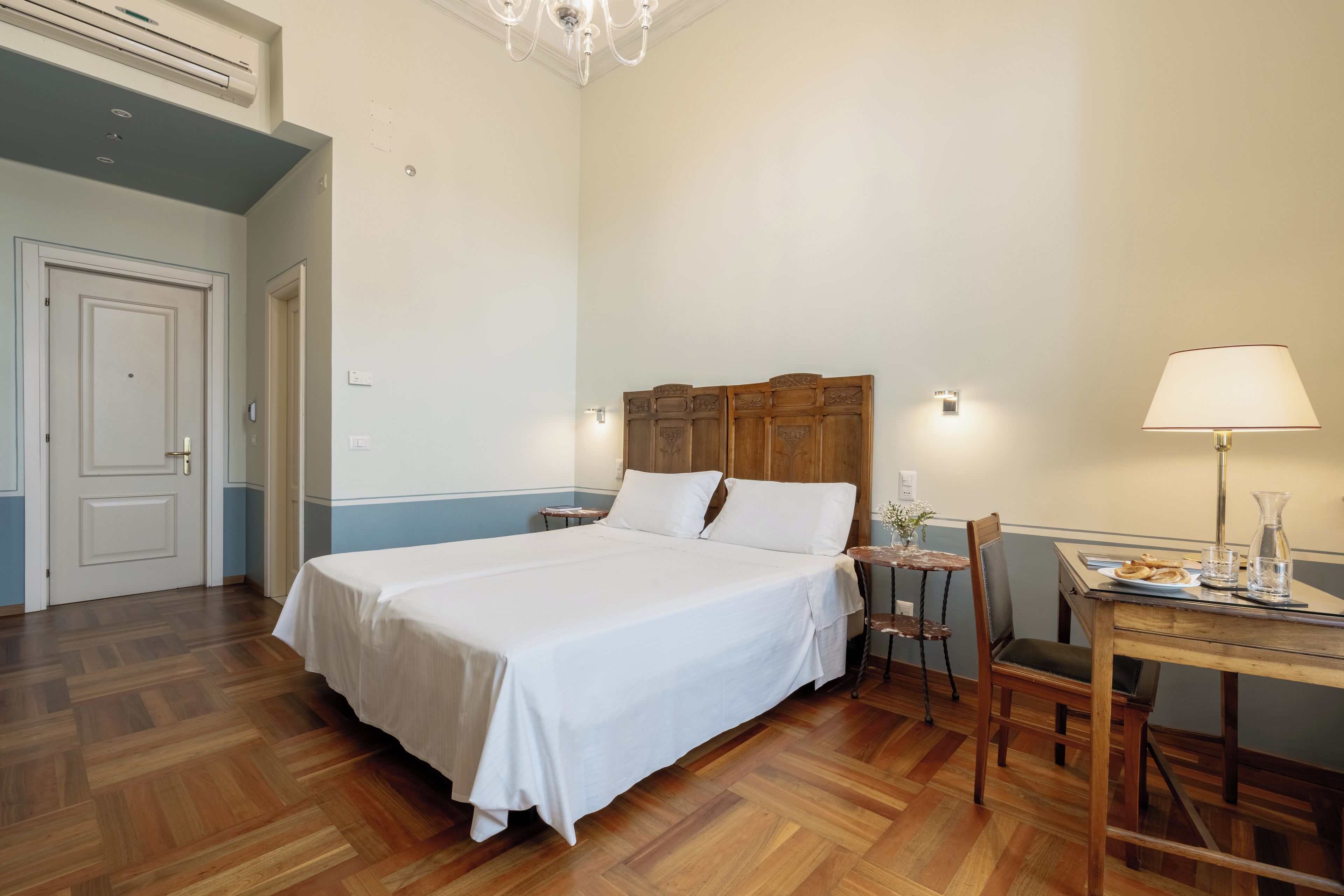 A hotel room with a large bed, a wooden headboard, a desk with a chair, and a lamp.