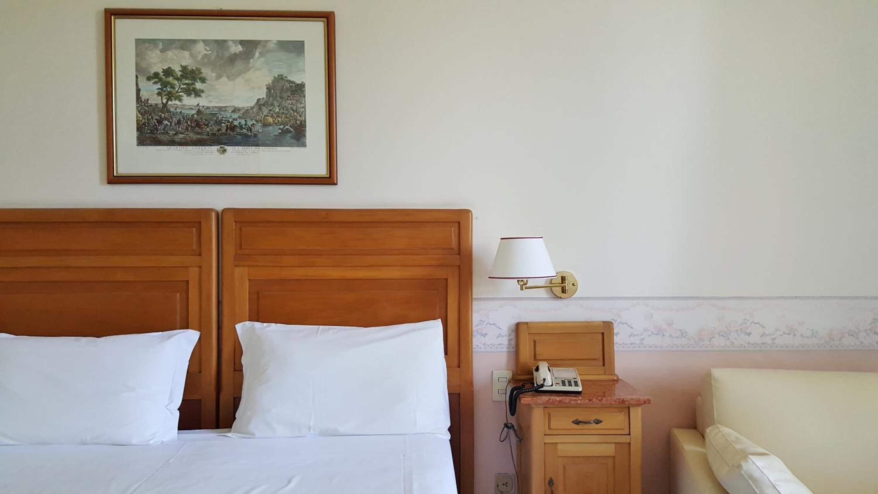 A hotel room with a double bed, a bedside table with a lamp, a phone, and a small cabinet.