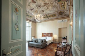 Une chambre d’hôtel avec un grand lit, un canapé, un lustre et un plafond décoratif.