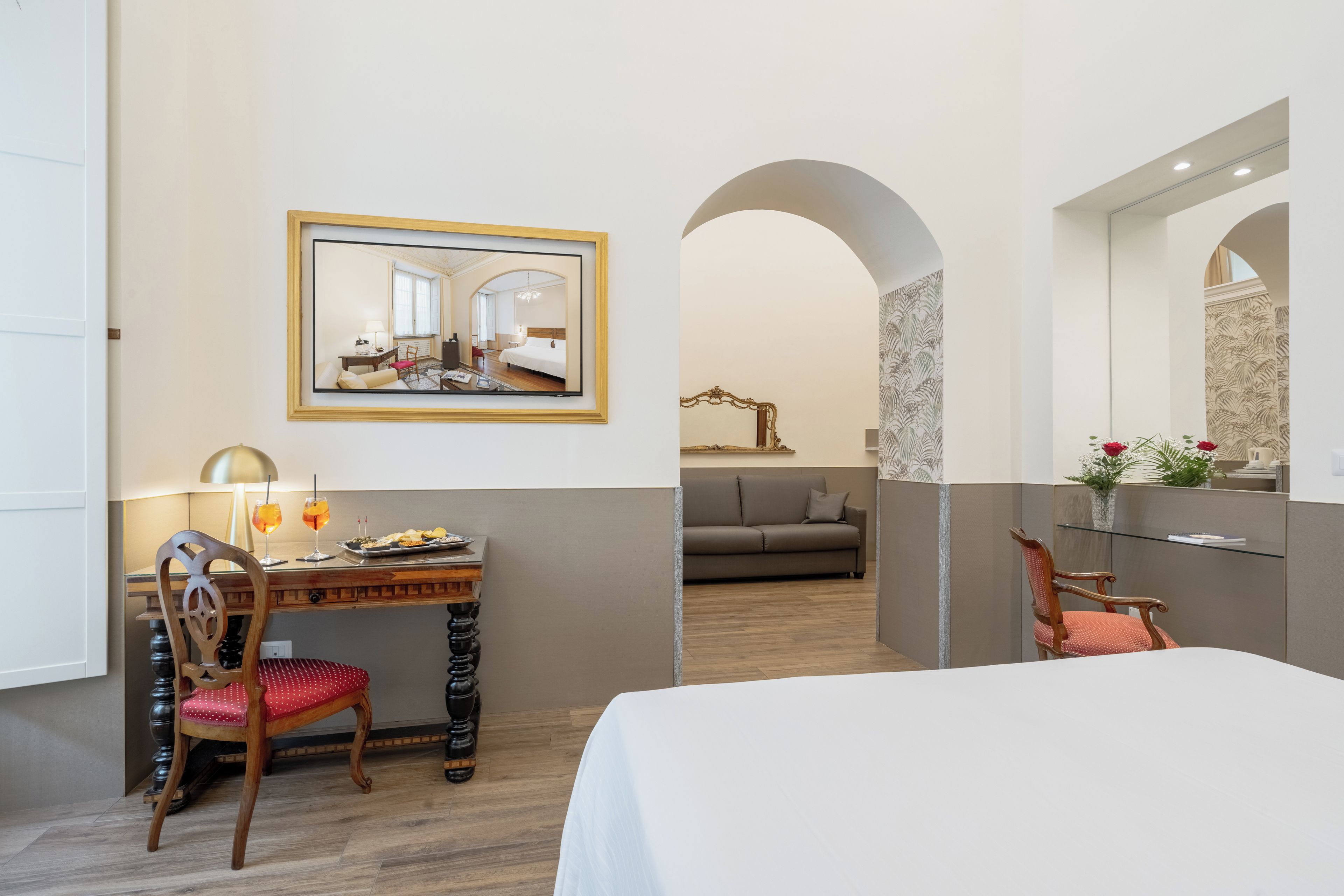 Habitación de hotel con cama, escritorio con silla, espejo y vista al pasillo.