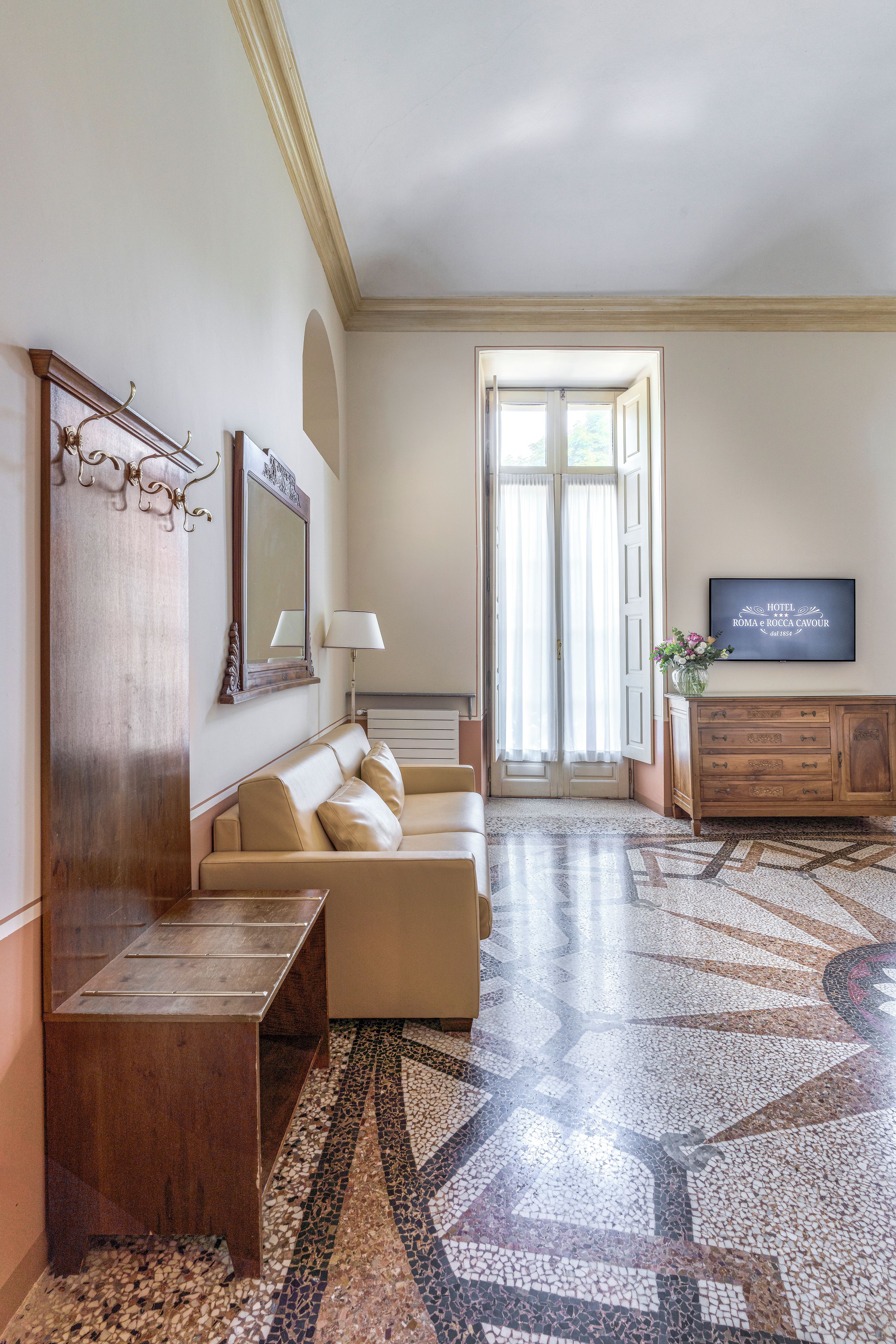 Habitación de hotel con sofá, un armario de madera, televisor y una ventana grande con cortinas.