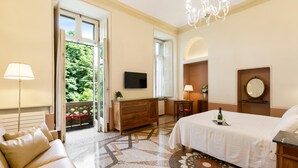 Ein Hotelzimmer mit Bett, Fernseher, einer Kristallleuchtre, einem Schreibtisch und Blick auf Grünflächen.