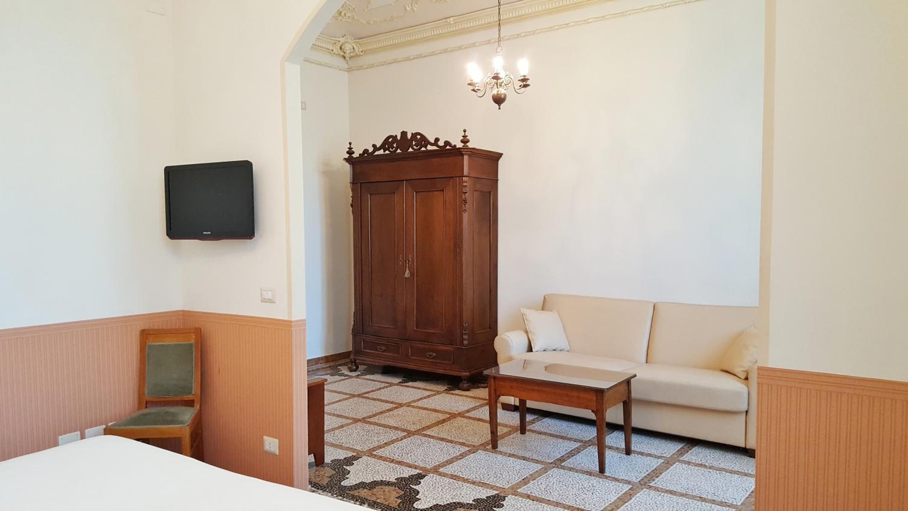 Ein Zimmer mit einer Couch, einem Holzschrank, einem an der Wand befestigten Fernseher und einem gemusterten Boden.
