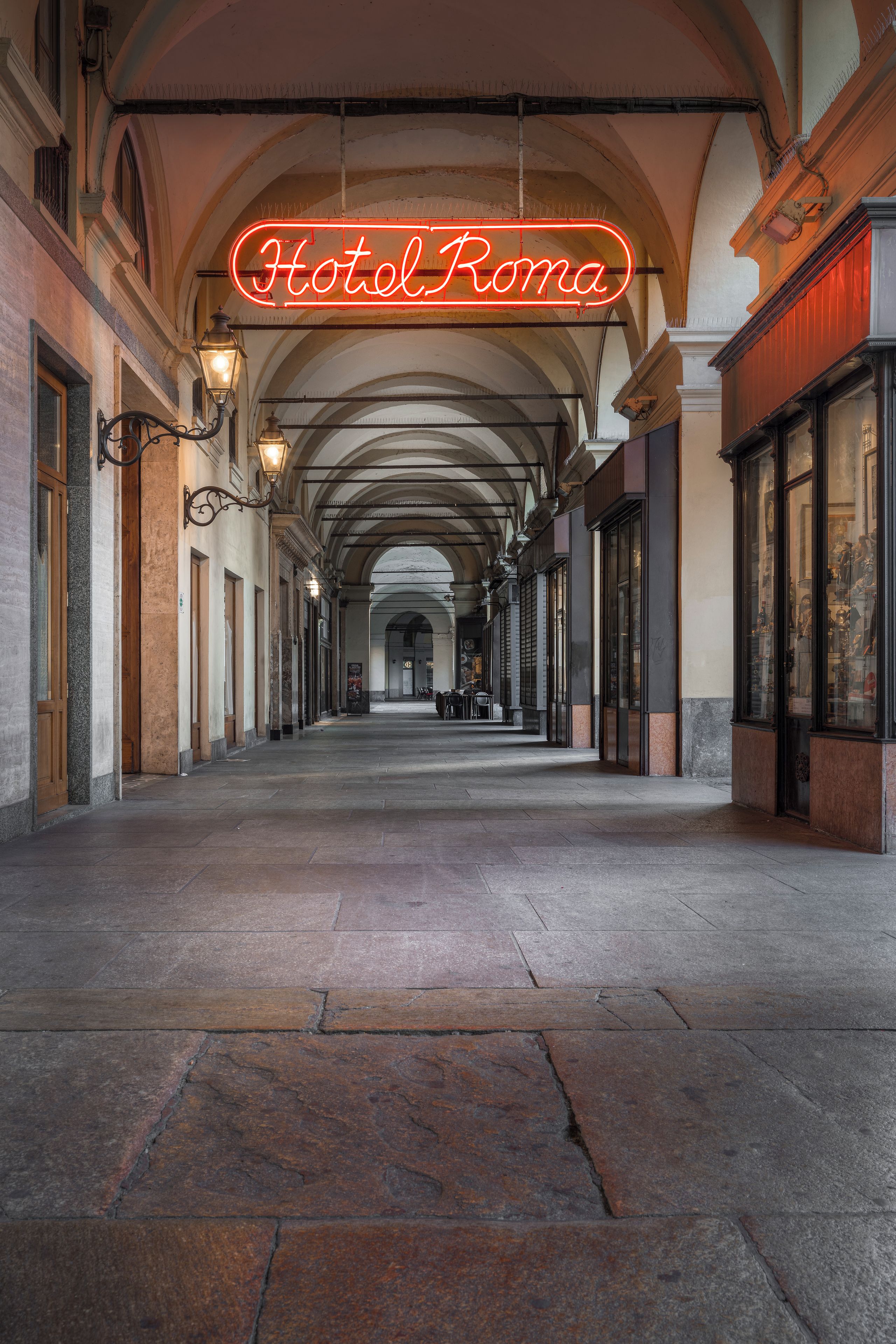 Un corridoio con un neon che recita 'Hotel Roma' e soffitti a volta.