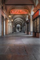 Un corridoio con un neon che recita 'Hotel Roma' e soffitti a volta.