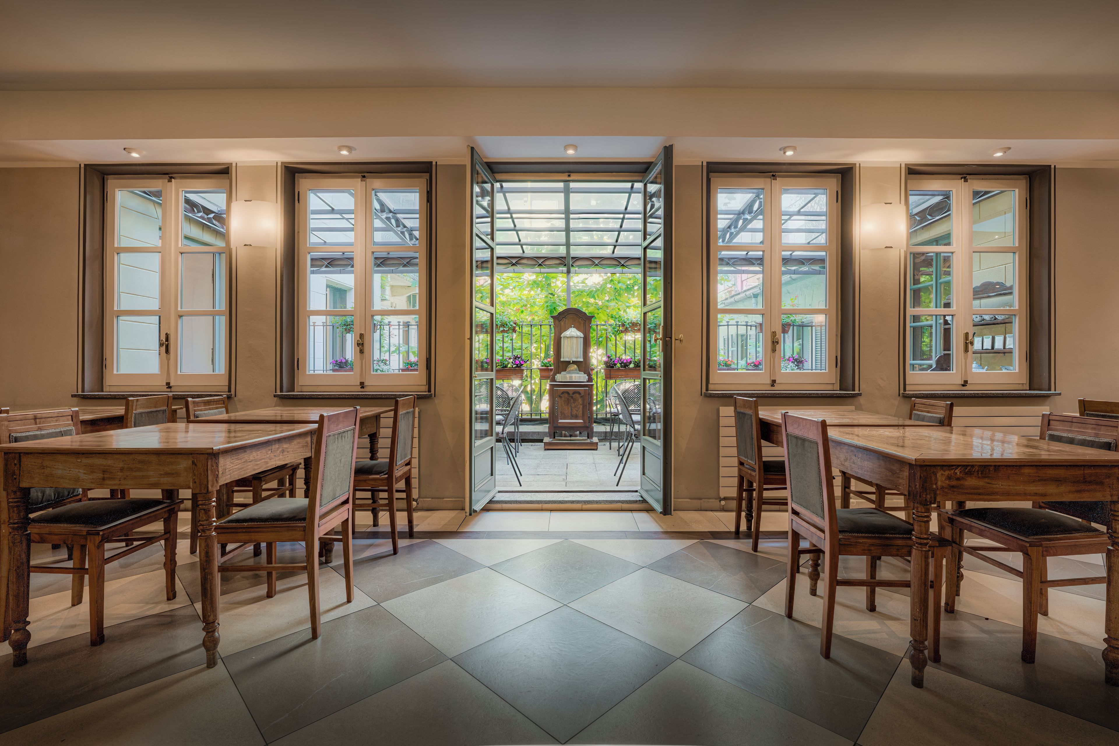 Un comedor con mesas y sillas de madera, y un ventanal que da a un jardín exterior.