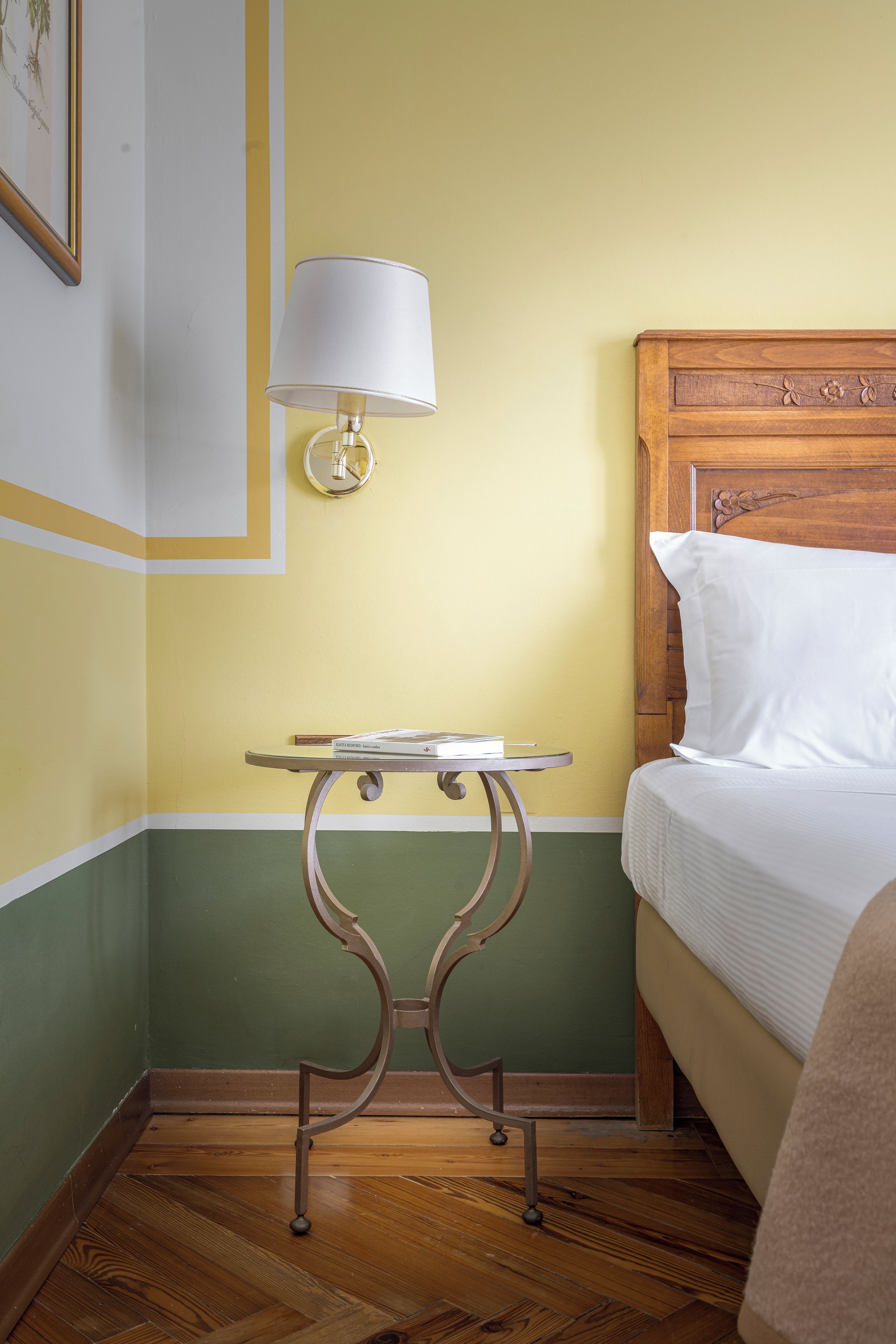 A hotel room with a bed, a bedside table with a lamp, and a small table with a book.