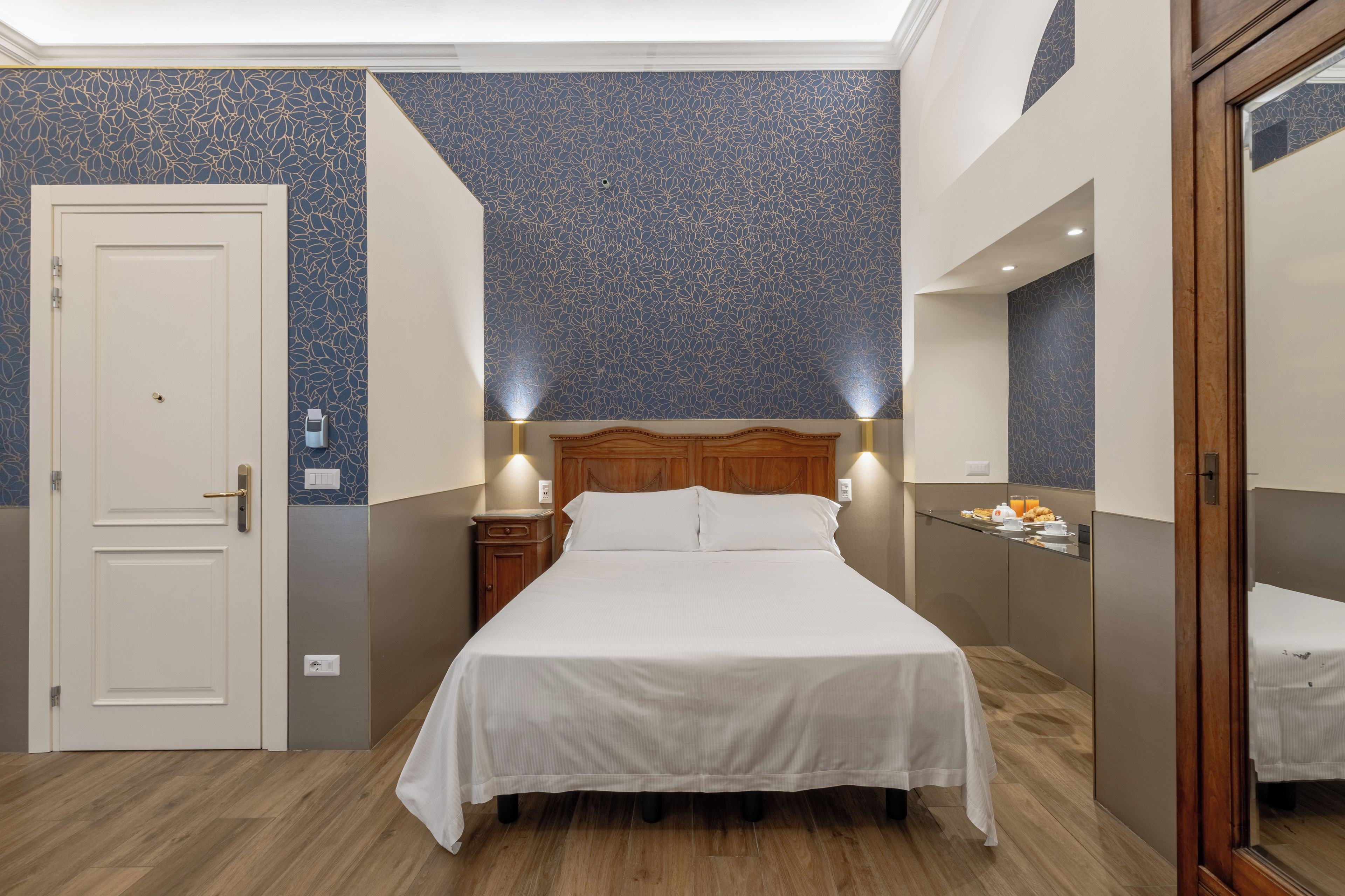 A hotel room with a bed, bedside tables, a wardrobe, and a bathroom mirror.