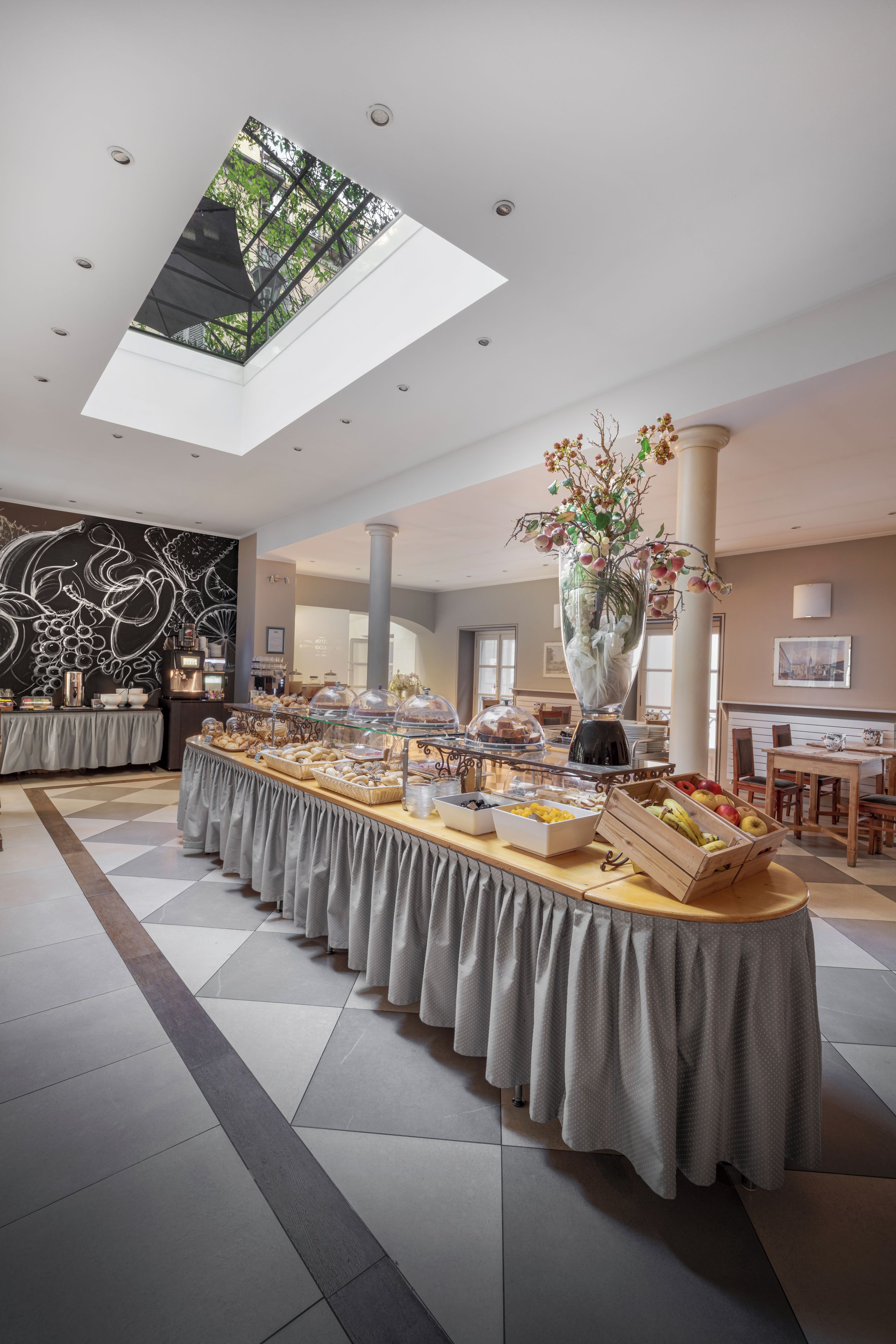 Una habitación de hotel con bufé de desayuno, tragaluz y un gran florero con flores.