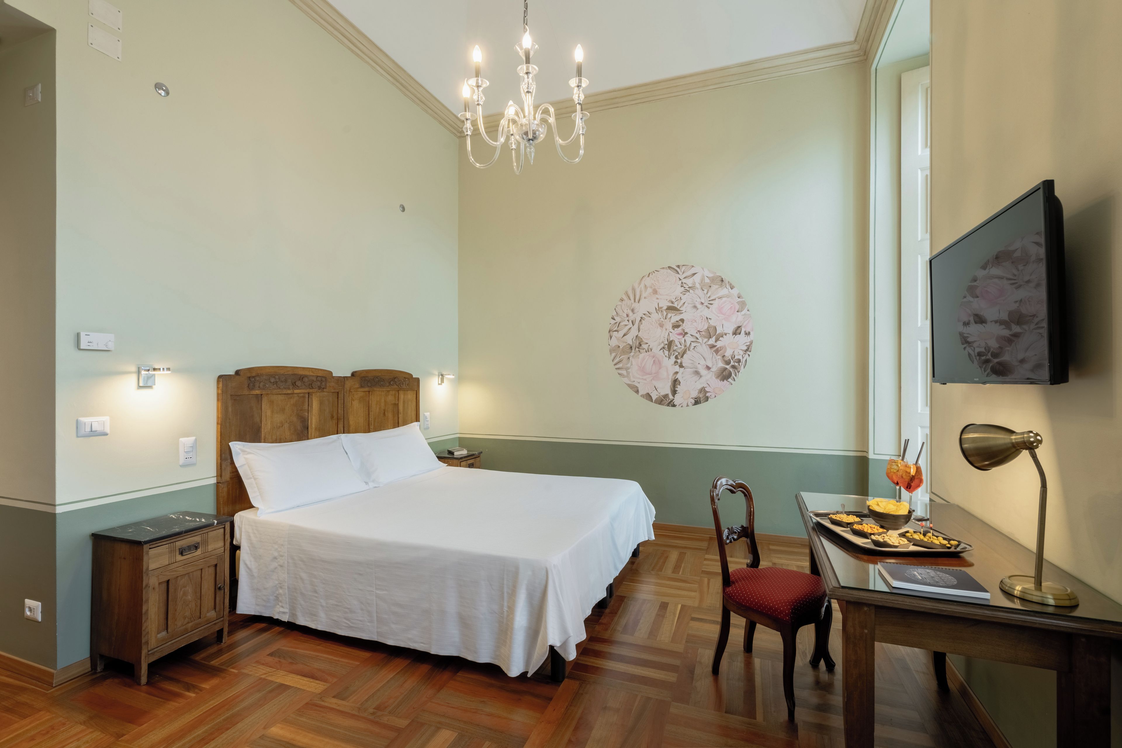 Una habitació d'hotel amb un llit, un escriptori amb una cadira, una televisió i una làmpada penjant.
