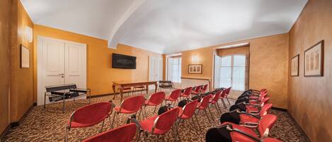 Un salón de conferencias con filas de sillas rojas, una mesa de madera y una puerta blanca.