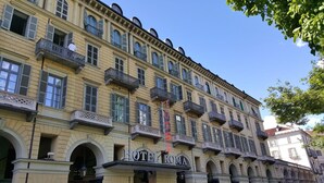 Ein mehrstöckiges Gebäude im klassischen Stil, mit Balkonen und Rundbogenfenstern. Am Gebäude ist ein Schild mit der Aufschrift "HOTEL ROMA" angebracht.