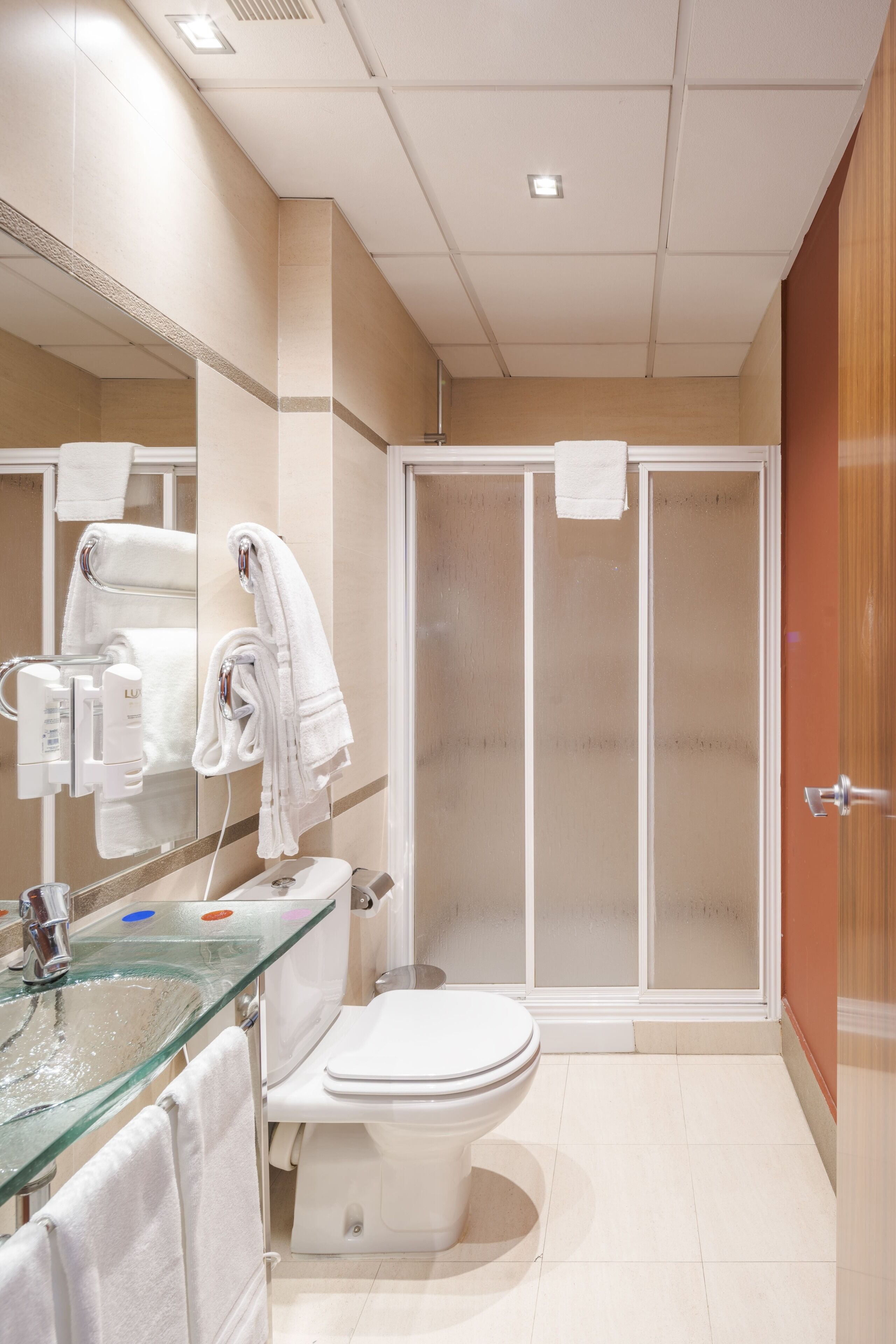 Et moderne badeværelse med vask af glas, hvid toilet og brusekabine med glasvægge.