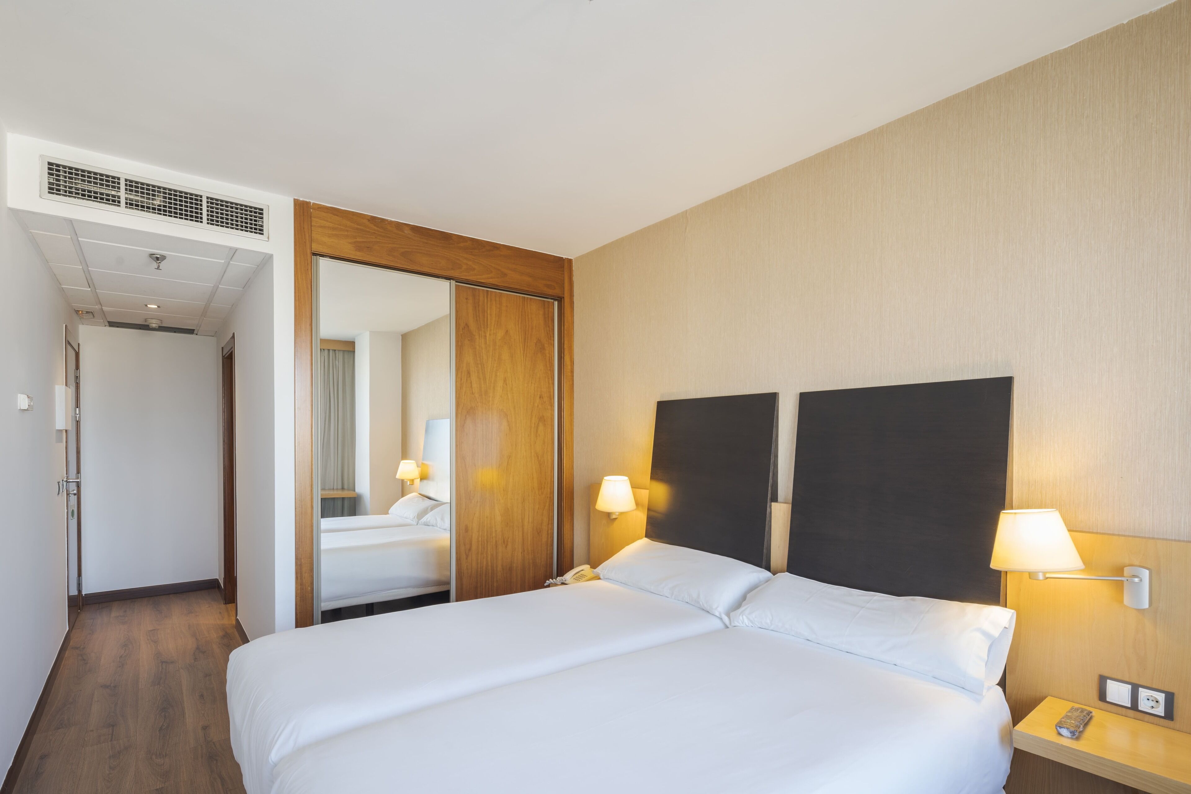 Una habitación de hotel con una cama grande, un armario de madera, un espejo y dos lámparas de noche.