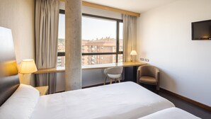 A hotel room with a large bed, a desk, two chairs, a TV, and a window with curtains. - Hotel Rice Bulevar (Burgos)