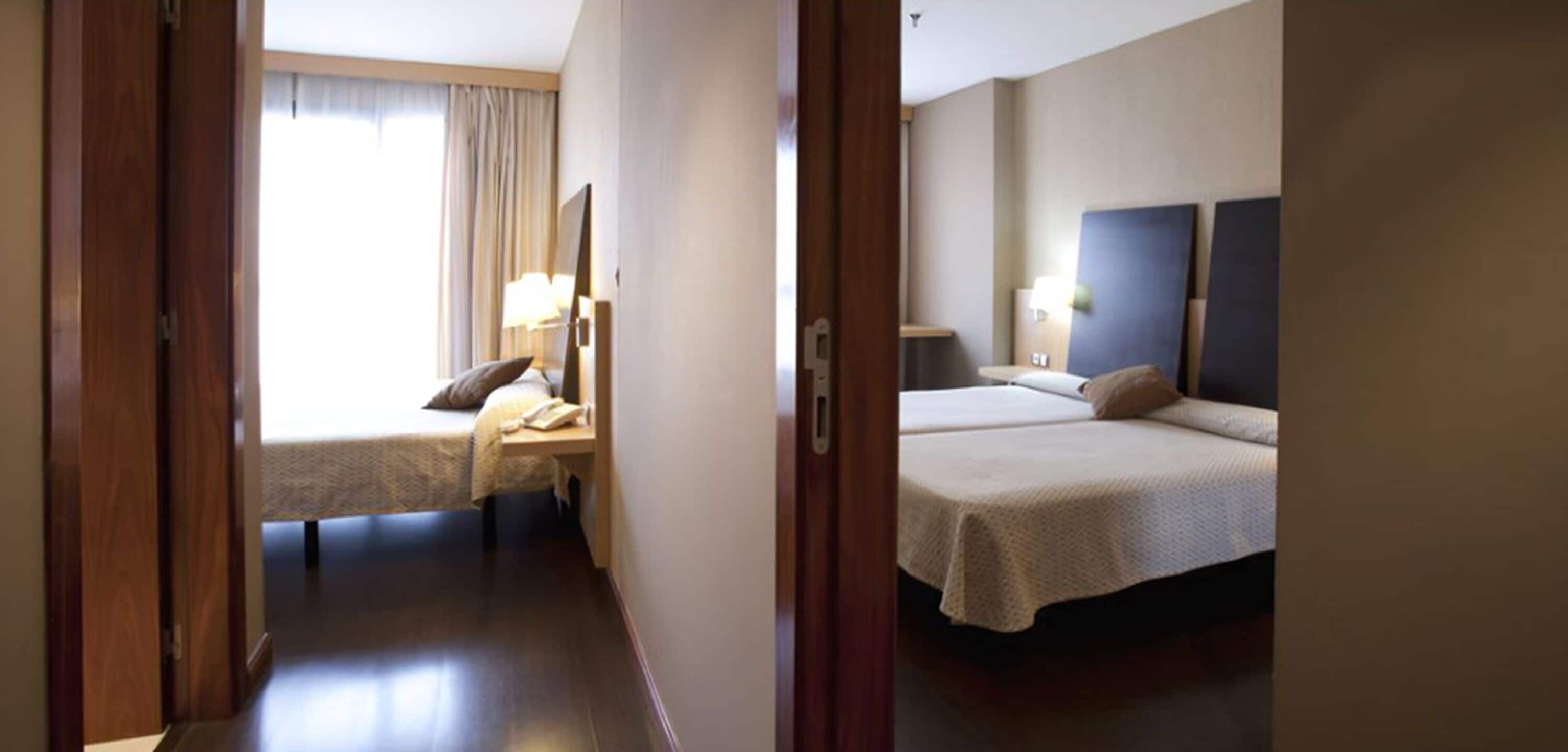 Una habitación de hotel con cama, mesita de noche, lámpara y vistas al exterior.