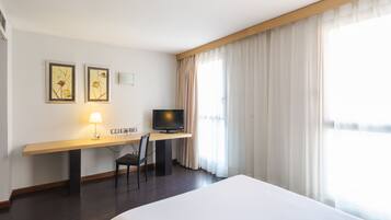 A hotel room with a large bed, a desk with a television, two framed pictures, and a lamp.