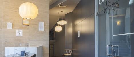 Un moderno vestíbulo de hotel con una recepción, iluminación colgante y una pared de vidrio que anuncia un área de café con WiFi.