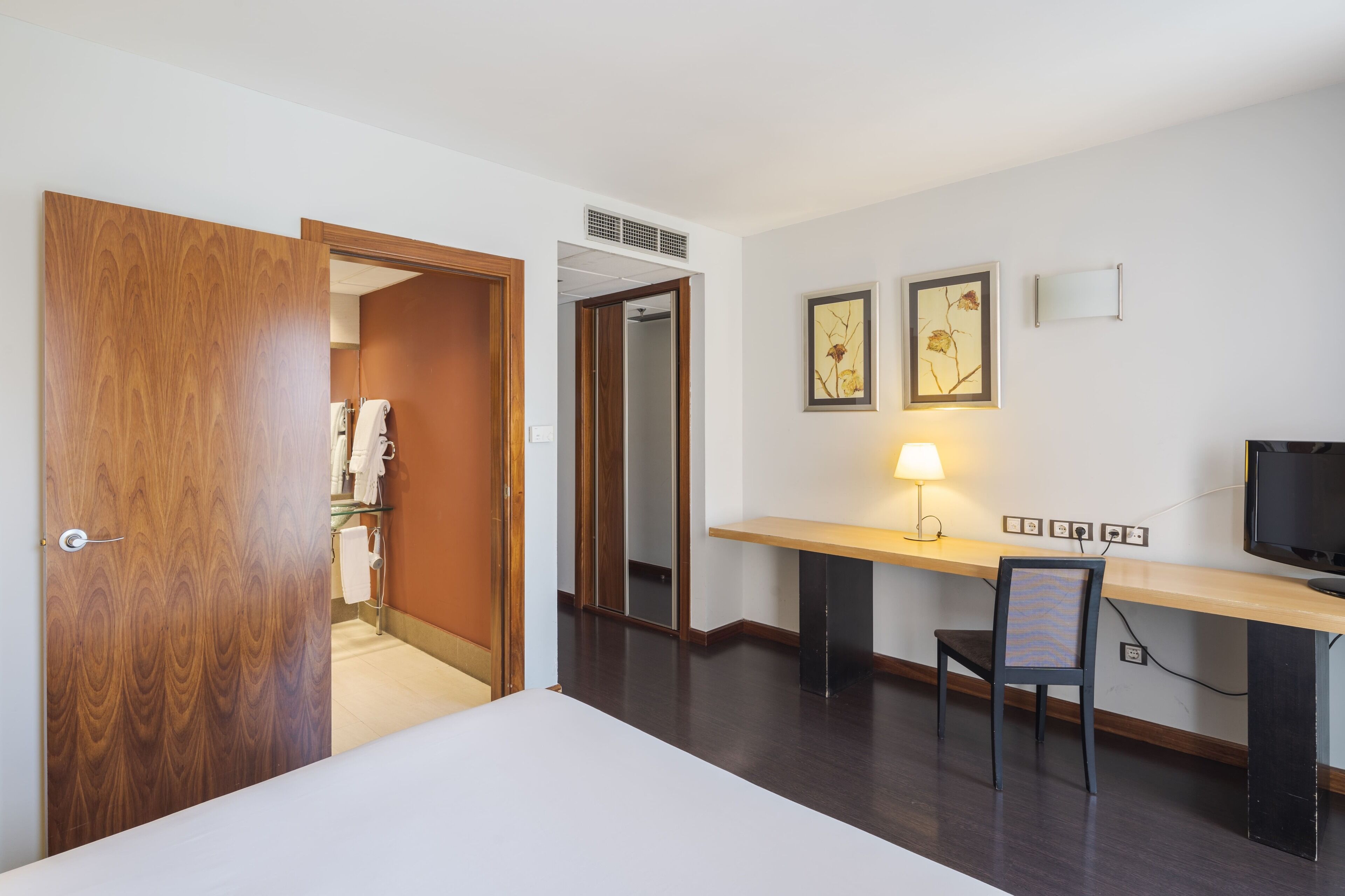 Une chambre d’hôtel avec une porte en bois, un bureau avec une lampe, une chaise et un téléviseur.