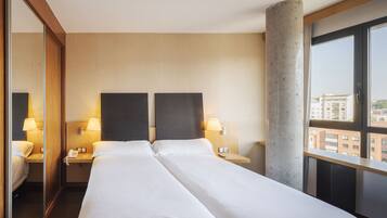 Ein Hotelzimmer mit zwei Betten, einem großen Fenster und Blick auf Gebäude.