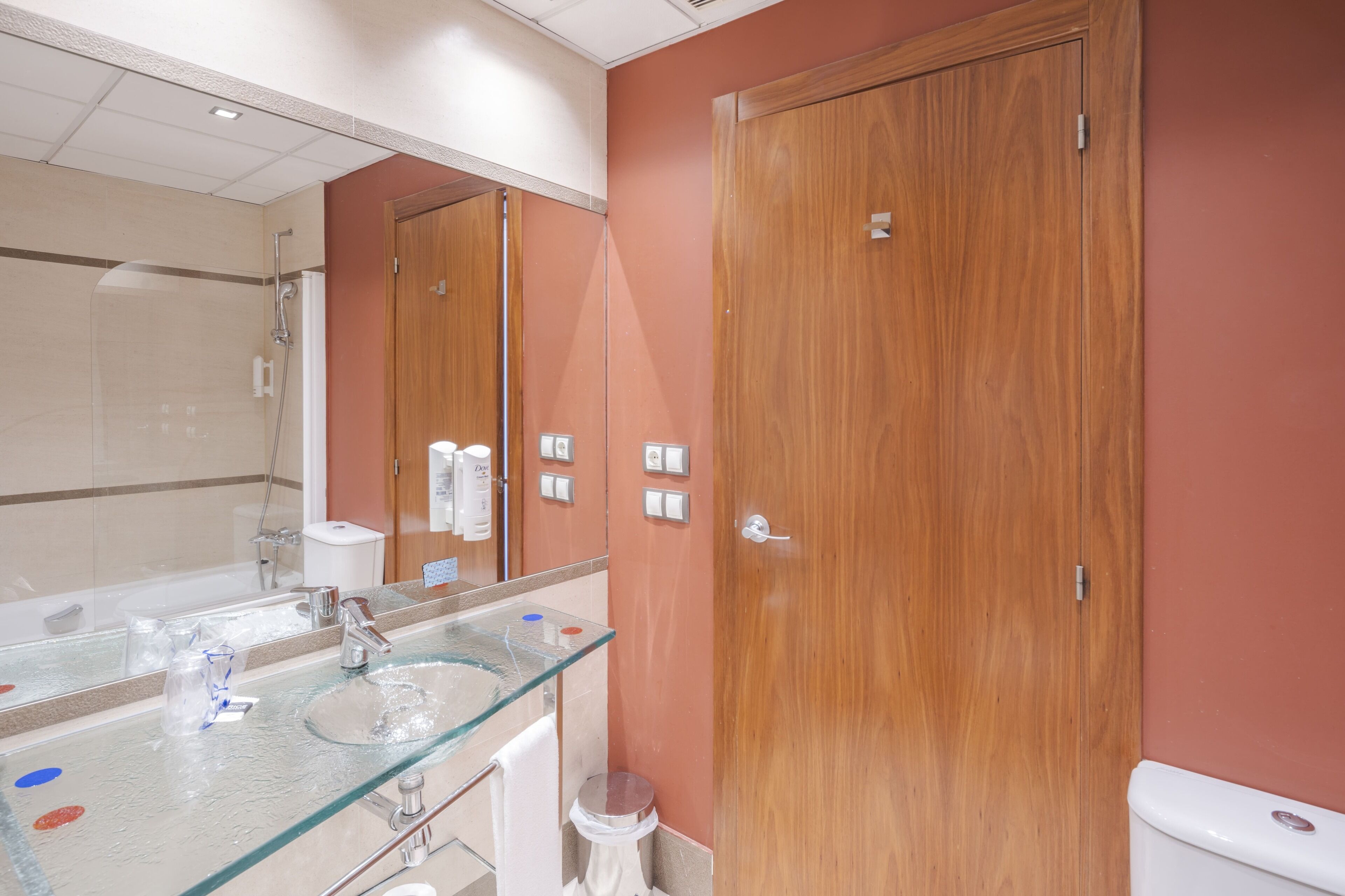 A bathroom with a glass sink, a shower, and wooden doors.