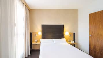 A hotel room with a large bed, two bedside tables with lamps, a wooden headboard, and a wooden wardrobe.