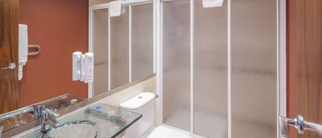 A bathroom with a glass sink, white toilet, and a shower enclosure.