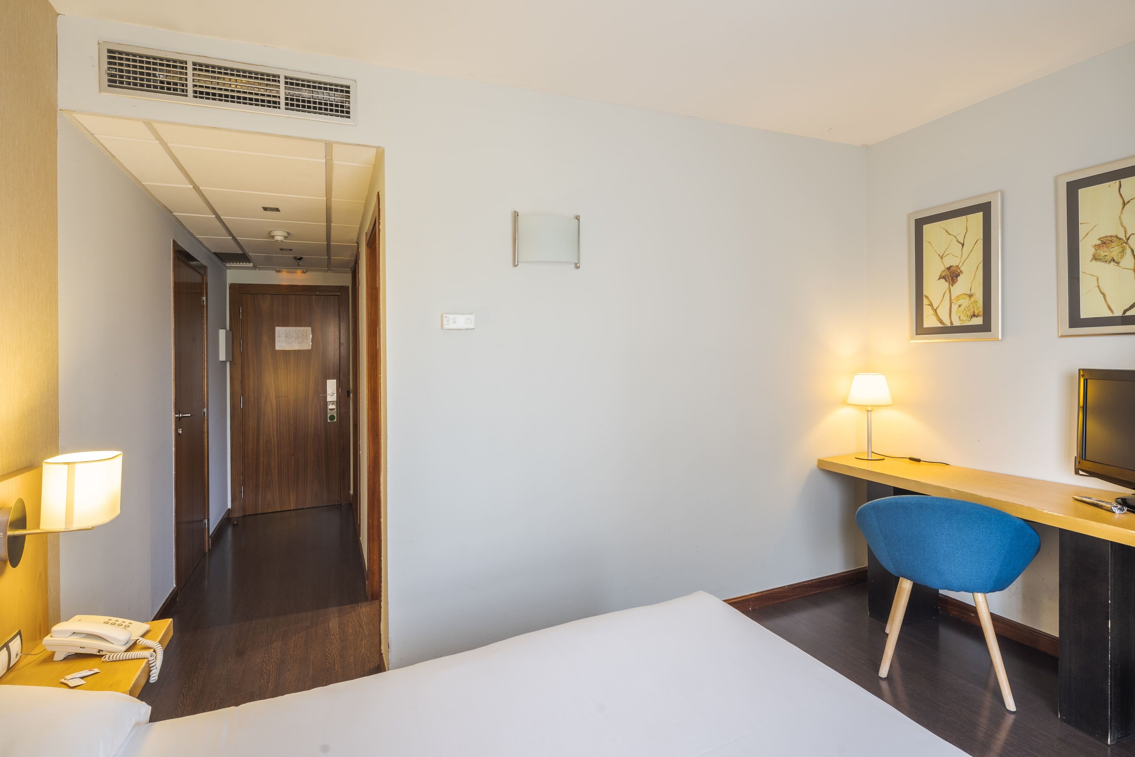 A hotel room with a bed, a desk with a chair, a lamp, a phone, and a TV.