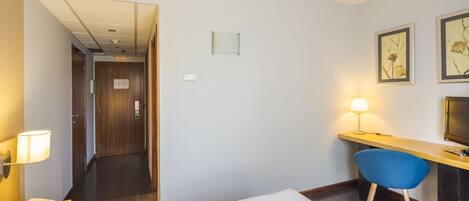 A hotel room with a bed, a desk with a chair, a lamp, a phone, and a TV.