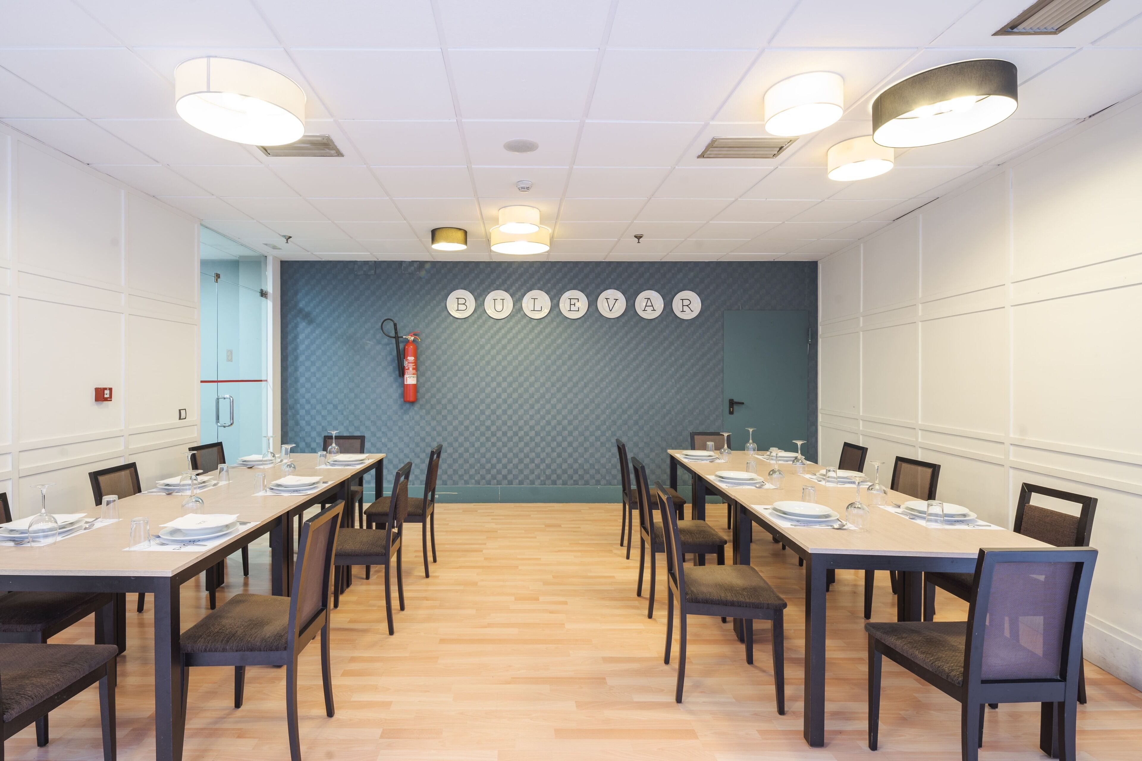 Une salle de conférence avec de longues tables, des chaises et un mur orné d’un motif bleu.