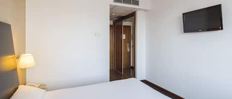Habitación de hotel con cama, lámpara de noche, teléfono, televisor montado en la pared y puerta que da a otra habitación.