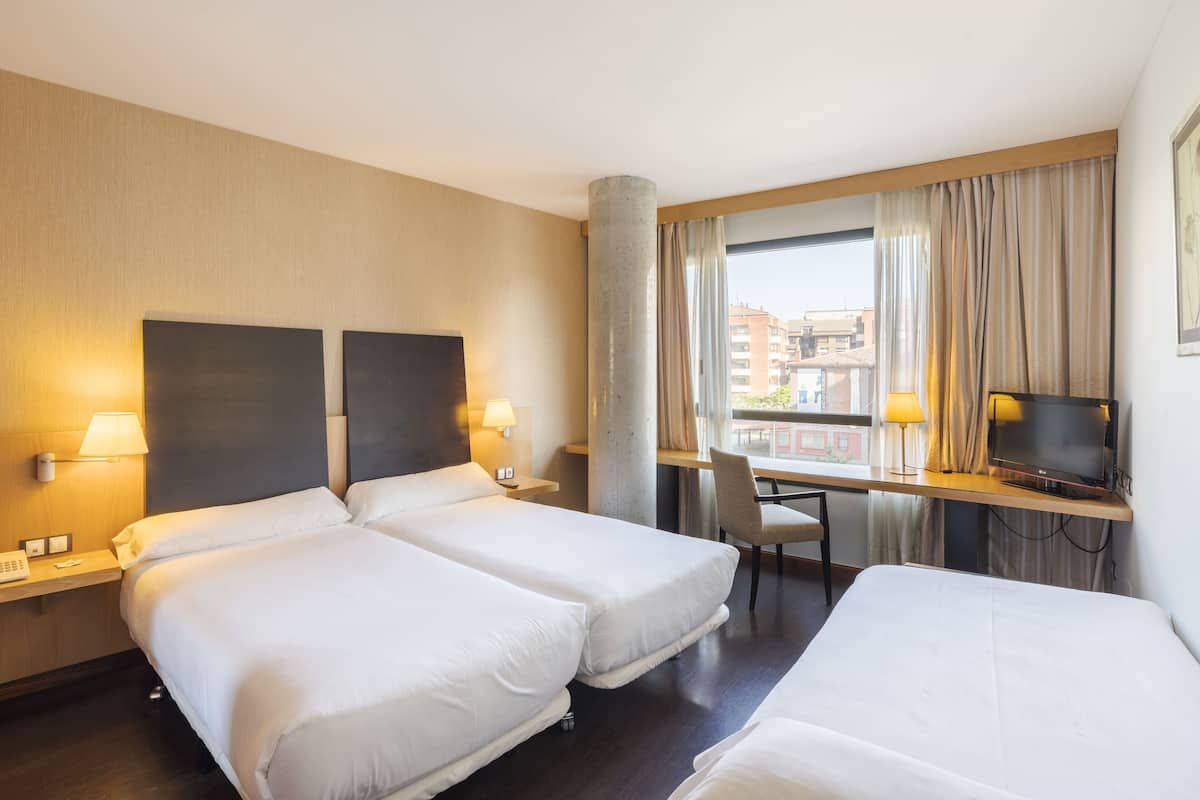 Une chambre d’hôtel avec deux lits, un bureau avec une télévision, une chaise et une fenêtre avec des rideaux.