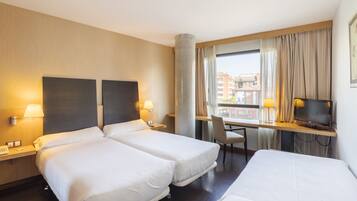 A hotel room with two beds, a desk with a TV, a chair, and a window with curtains.