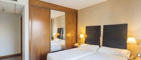 Una habitación de hotel con dos camas, un armario de madera, un espejo y lámparas de noche.