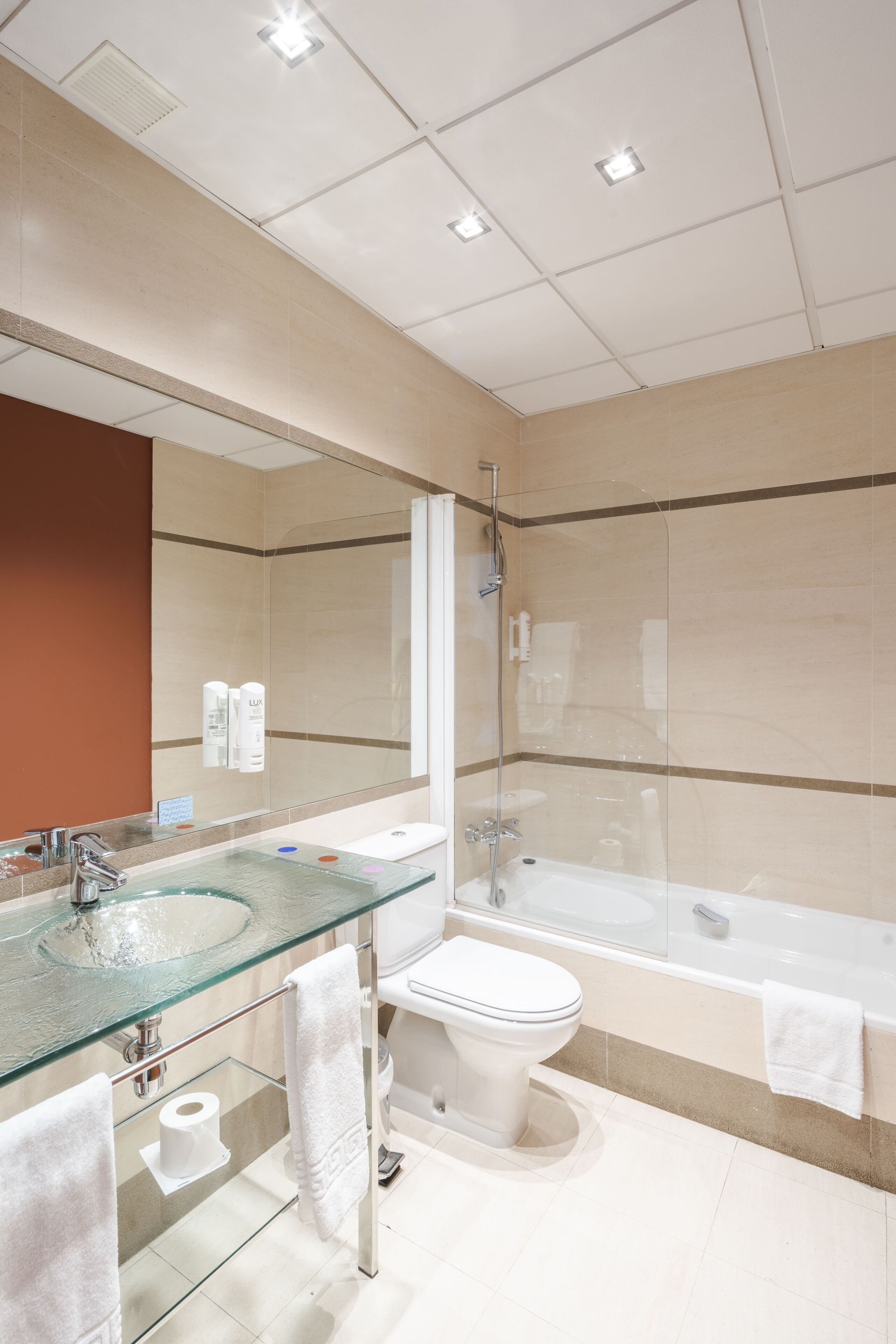 A modern bathroom with a glass sink, white toilet, and bathtub.