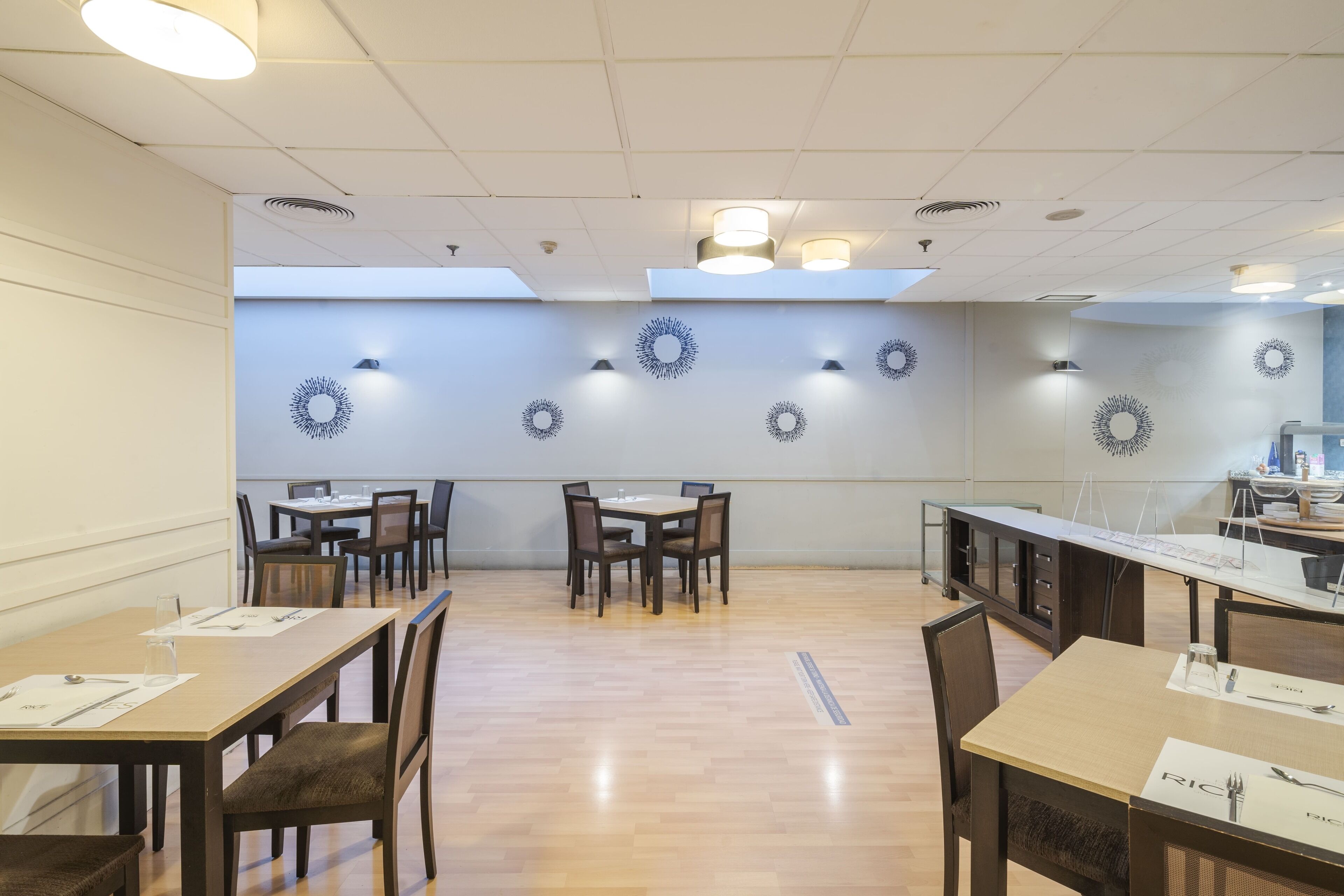 A dining area with multiple tables and chairs, ceiling lights, and decorative wall sconces.