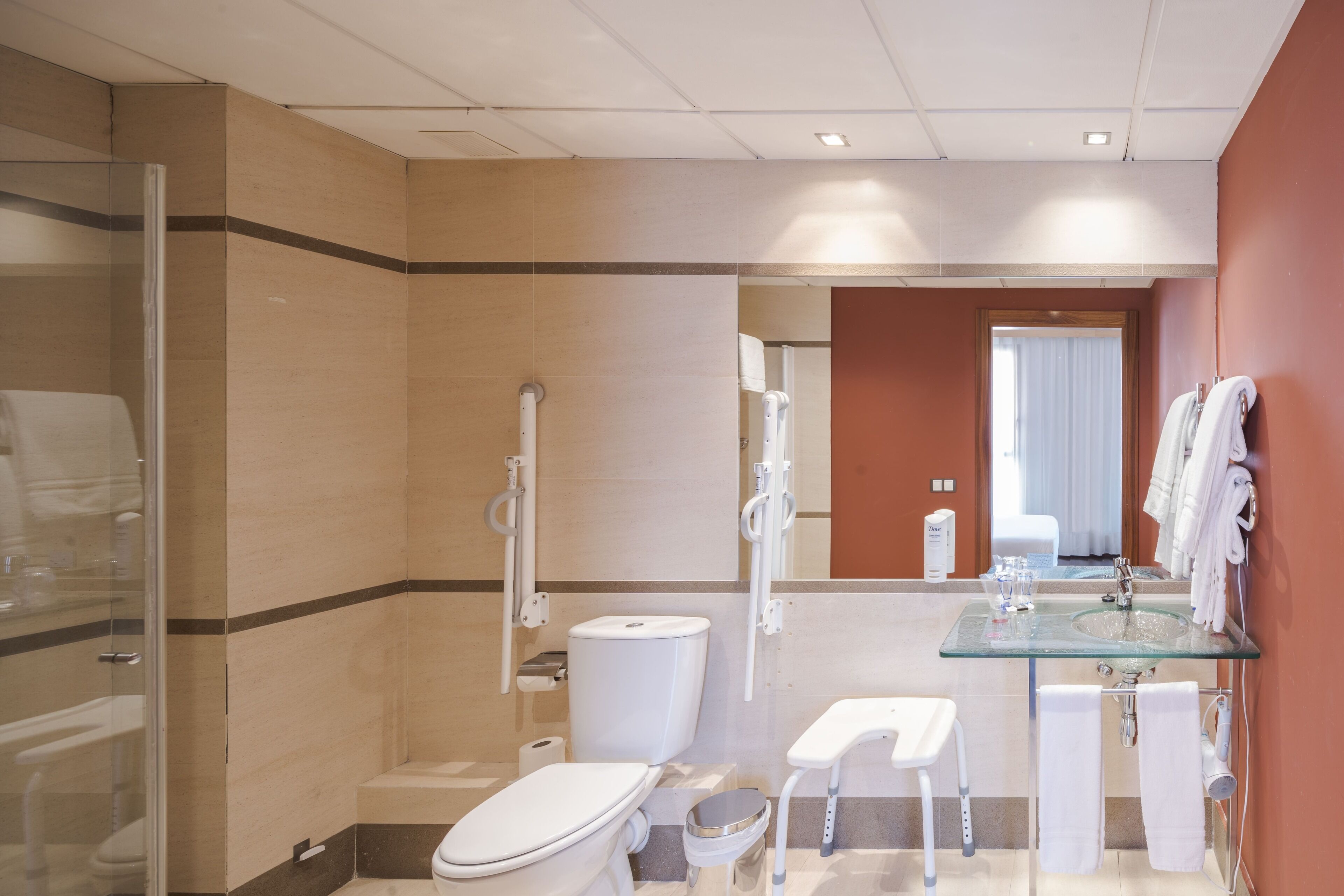 A modern bathroom with a glass sink, white fixtures, a glass shower enclosure, and a visible toilet.