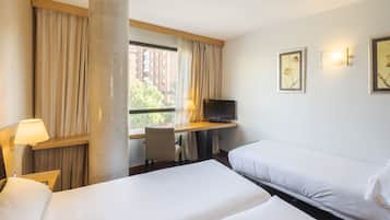 A hotel room with two beds, a desk with a TV, a lamp, and a large window with curtains.