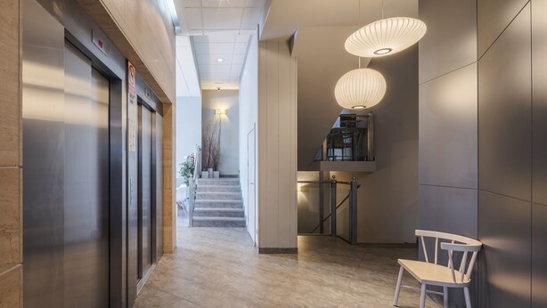A modern hotel lobby with a marble floor, a staircase, and a seating area with a white chair. - Hotel Rice Bulevar (Burgos)