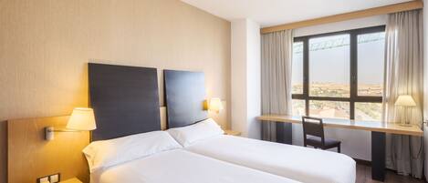 Habitación de hotel con dos camas, un escritorio, una silla, un teléfono y una ventana con vista a un puente.