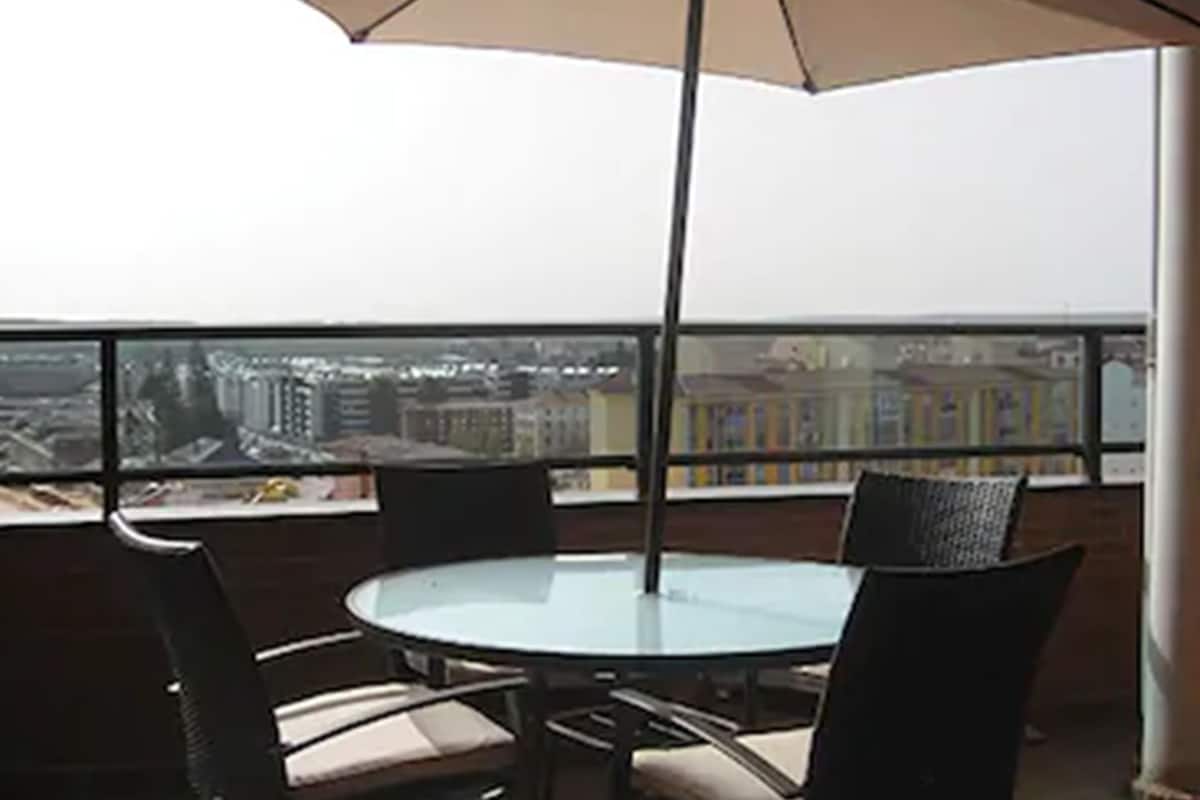 Une table ronde entourée de chaises et surmontée d’un grand parasol, le tout installé sur un balcon offrant une vue sur la ville.